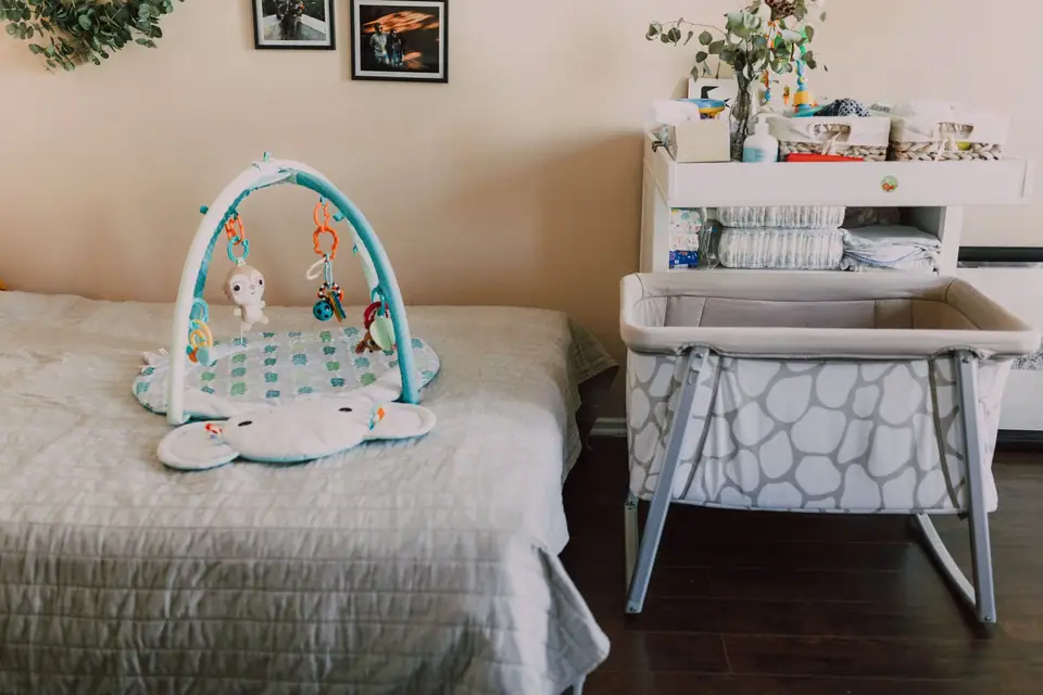 An empty mesh bassinet beside an adult bed, with a changing table behind it