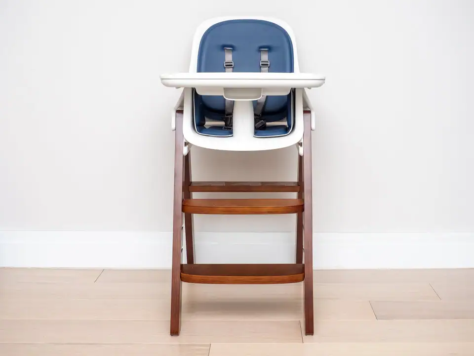 A wooden high chair with a white tray and a navy seat with a harness