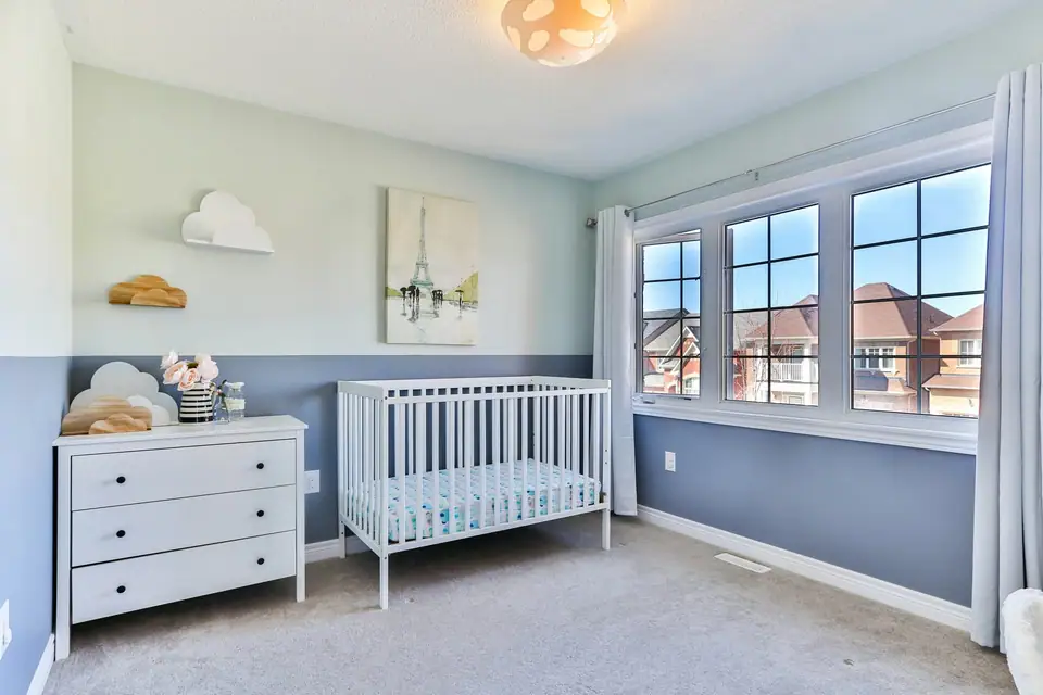 A bright nursery with a white chest of drawers and a crib holding only a fitted sheet