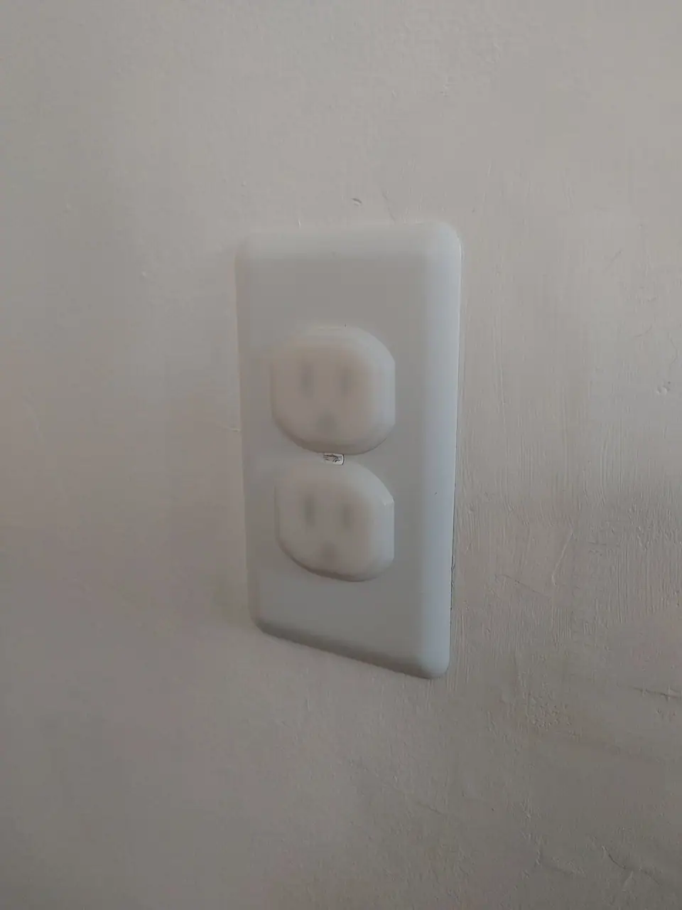 A wall outlet with white plastic plug covers pushed into both sockets