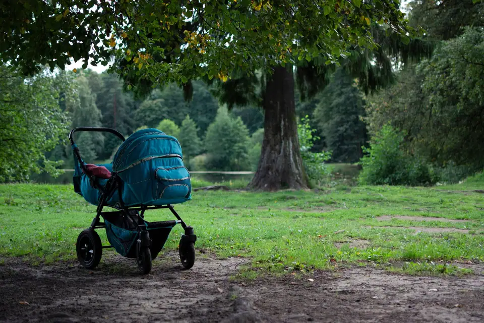 A teal pram parked on a dirt path under a tree in a park